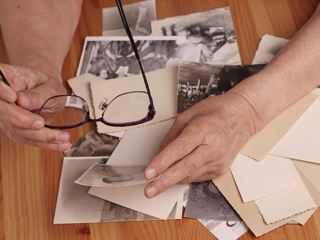 An elderly woman looks at old photographs, recalls her past youth. Hands on the table. Loneliness,, memories. An elderly woman looks at old photographs, recalls her past youth. Hands on the table. Loneliness, old age, memories.