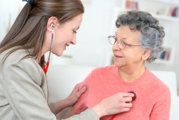 female caregiver examining senior woman with stethoscope Alzheimer's Community Care Near Sellersville, PA: How Important The 24-Hour Care Is For Your Parent