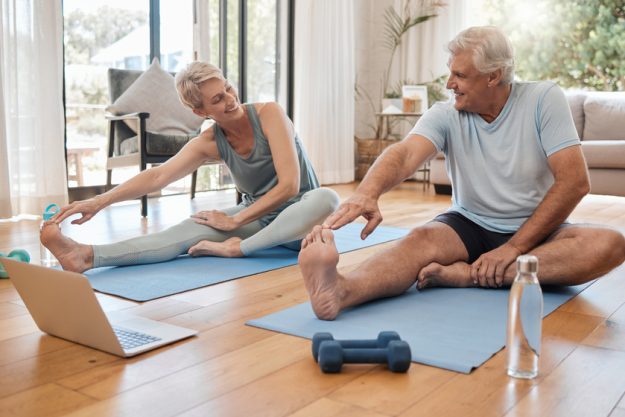 Stretching, fitness and senior couple with workout on the internet together on the living room floor. Happy, calm and healthy elderly man and woman training for wellness with exercise video on web 5 Stylish Amenities In Memory Care Community Near Doylestown, PA