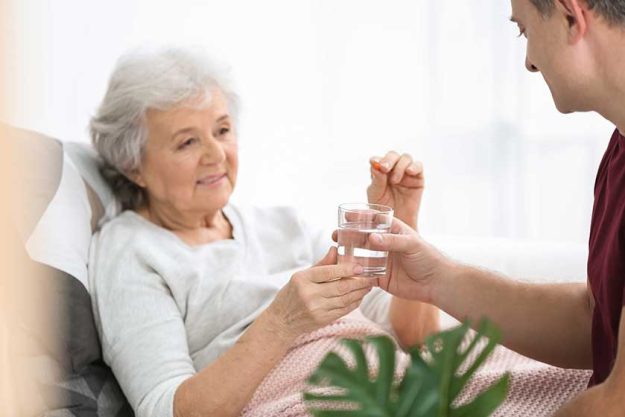 Man giving pill to elderly woman, indoors