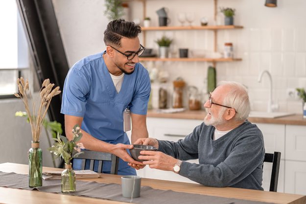 Smiling friendly caretaker serving breakfast to a pensioner