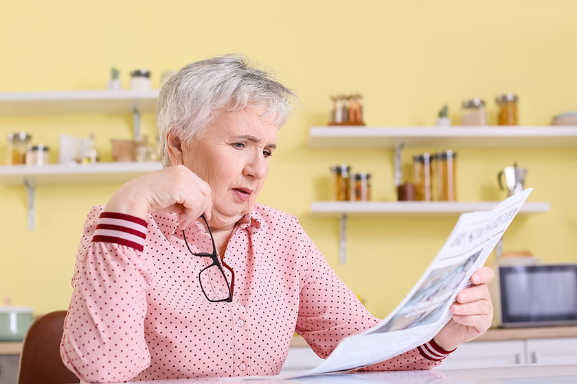 Stressed senior woman reading newspaper at home
