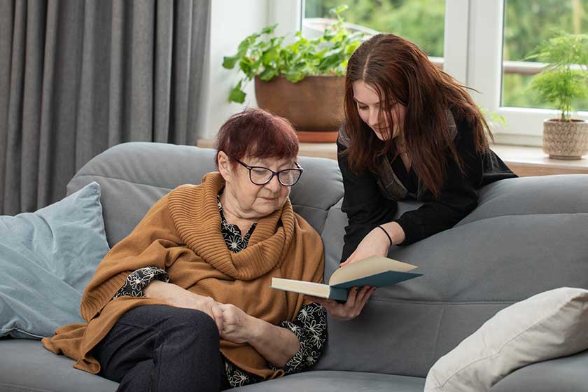 Senior woman and teenager girl reading book together. Grandmother and granddaughter reading book together at home.