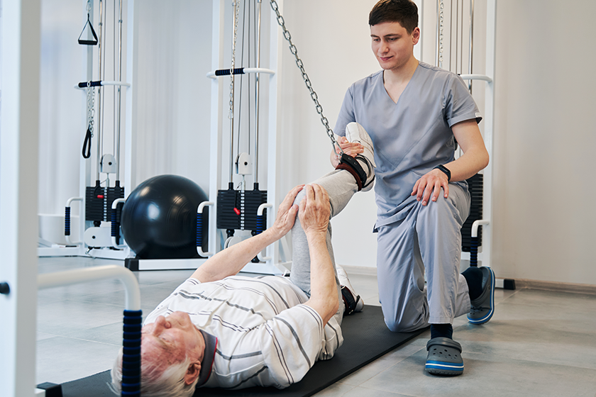 doctor-pulling-right-leg-of-pensioner-with-attached-resistance-band