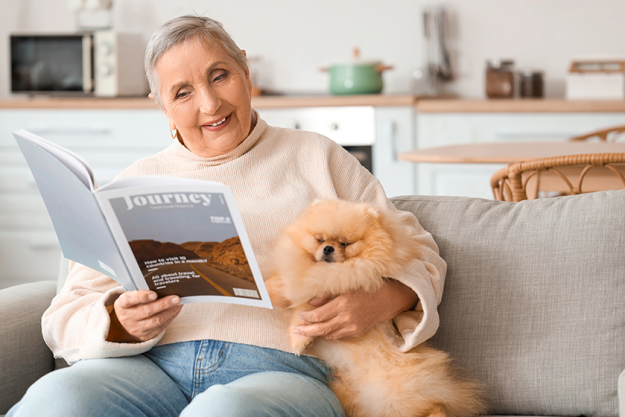 Senior woman with Pomeranian dog reading magazine